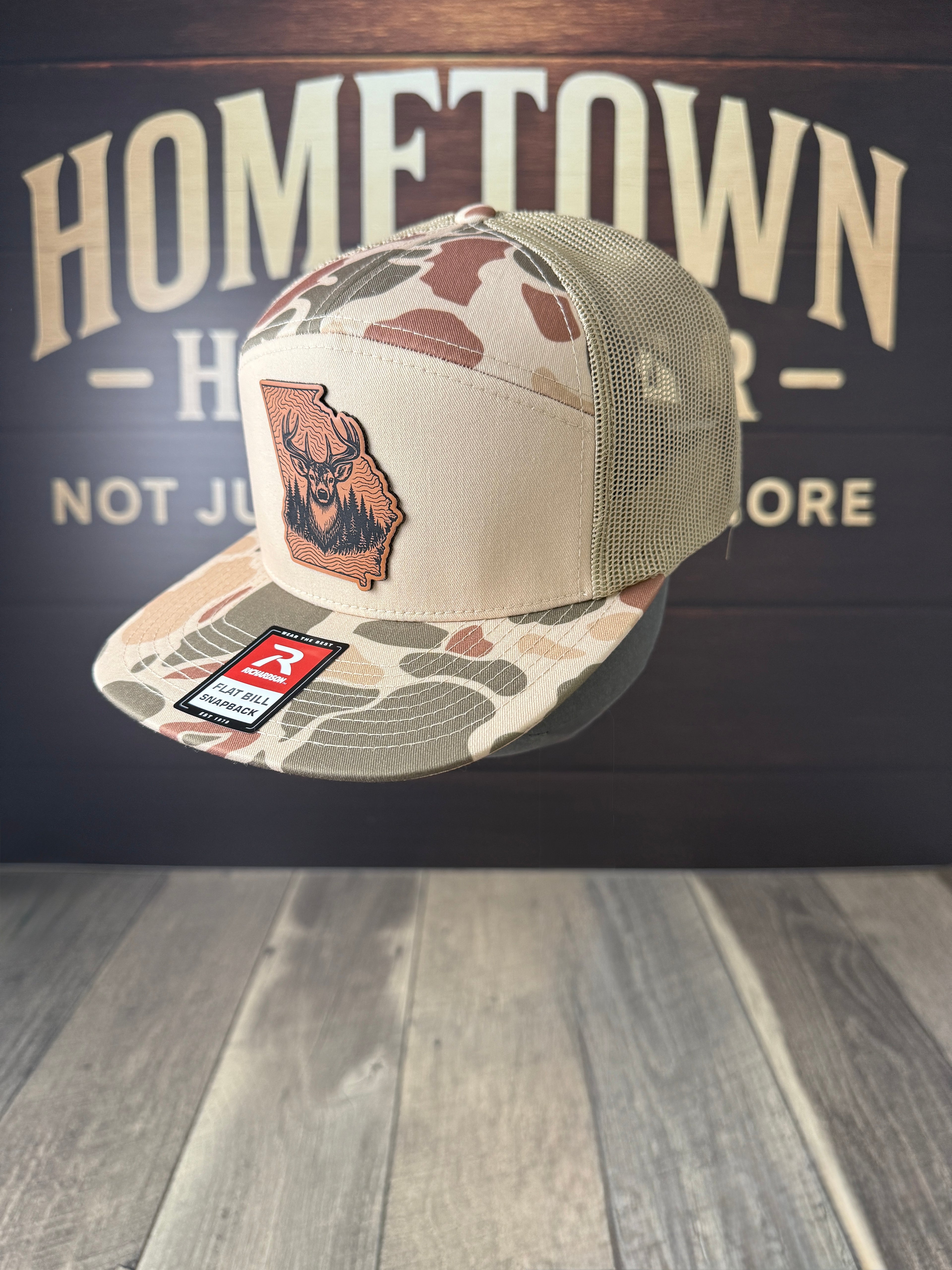 Camouflage cap with a logo on a wooden surface and background with 'Hometown' text.
