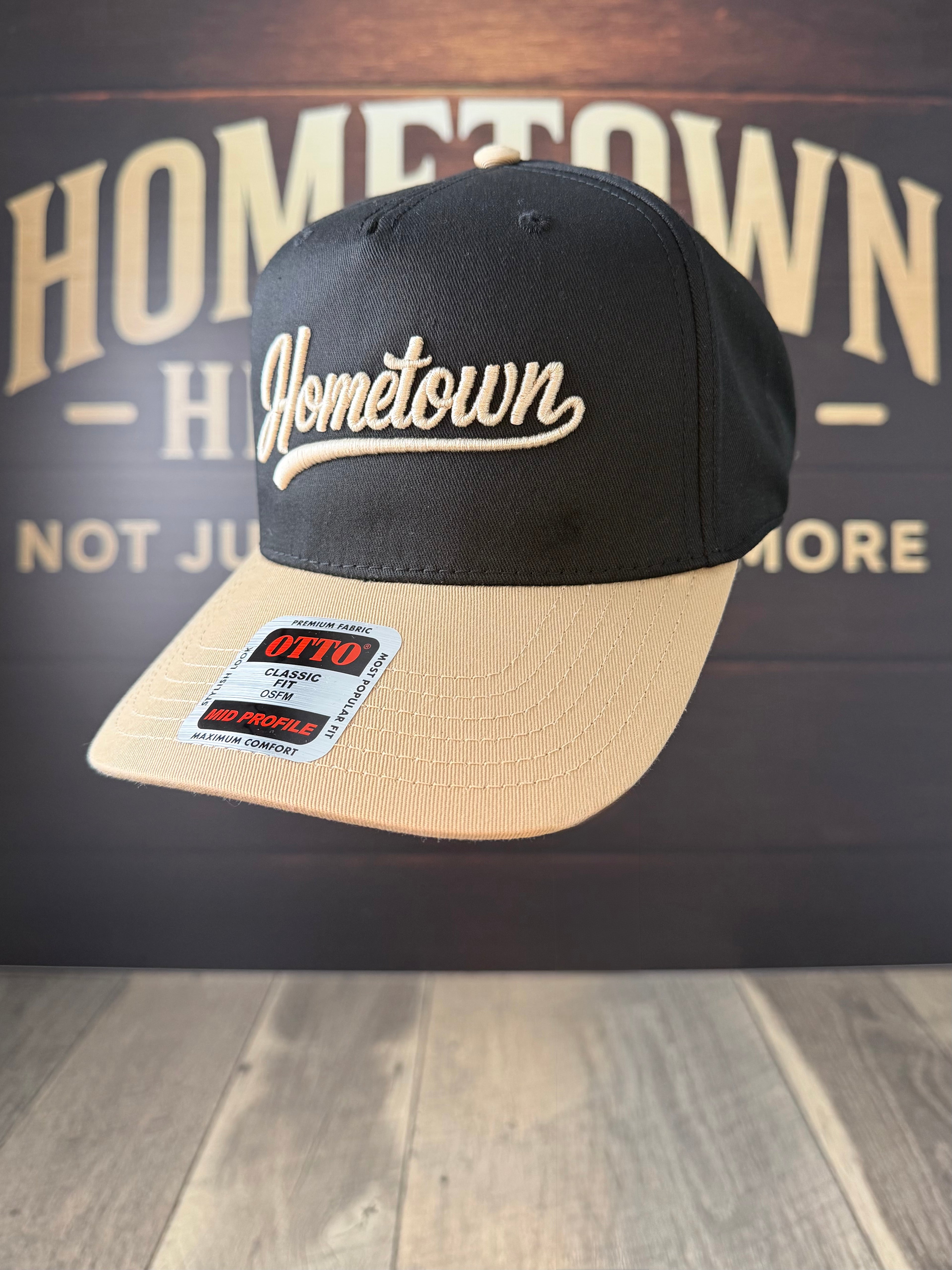 Black and Tan cap with 'Hometown' logo on a wooden surface with 'Hometown' branding in the background.