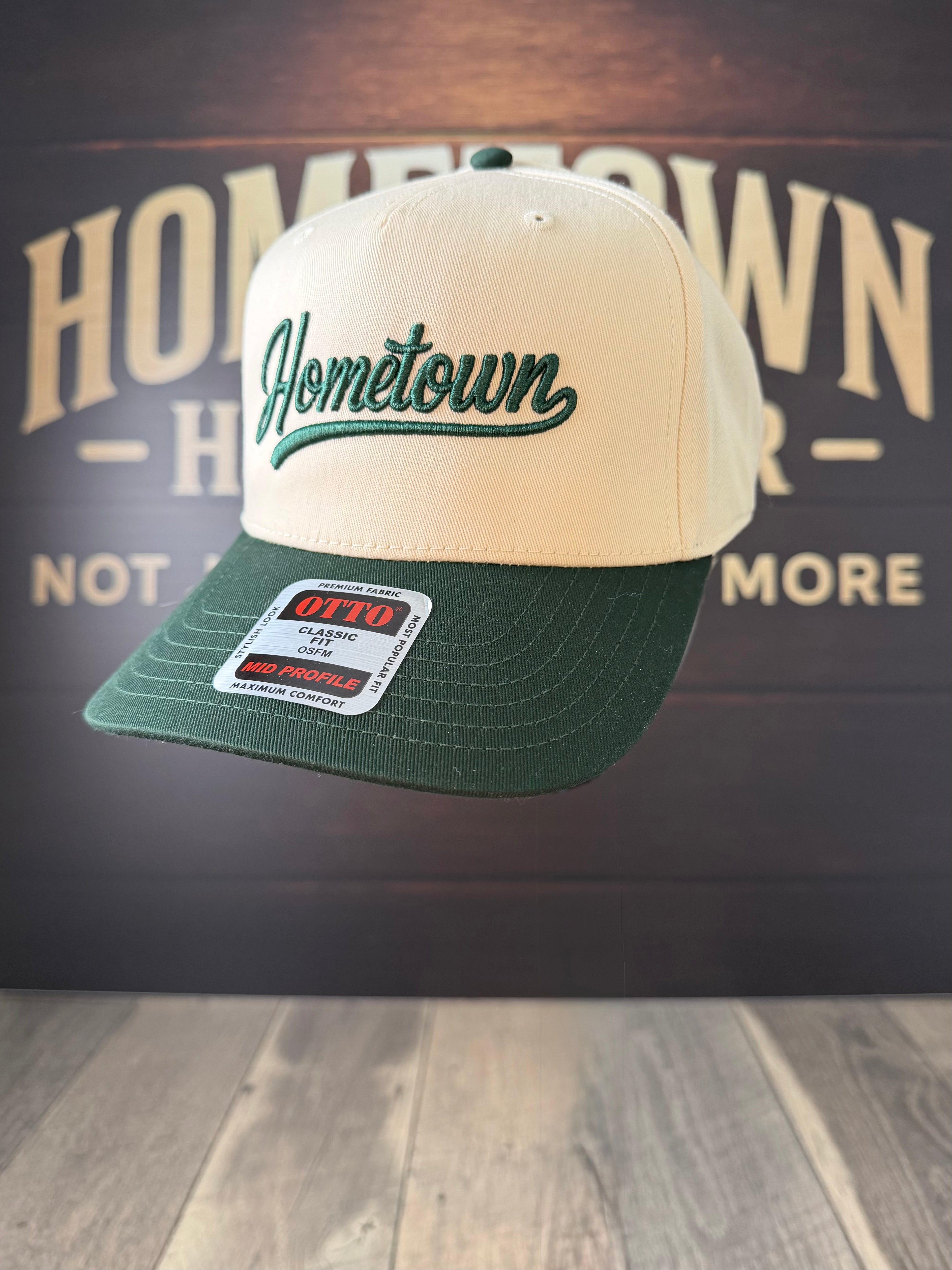 Beige and green cap with 'Hometown' text on a wooden surface and dark background.