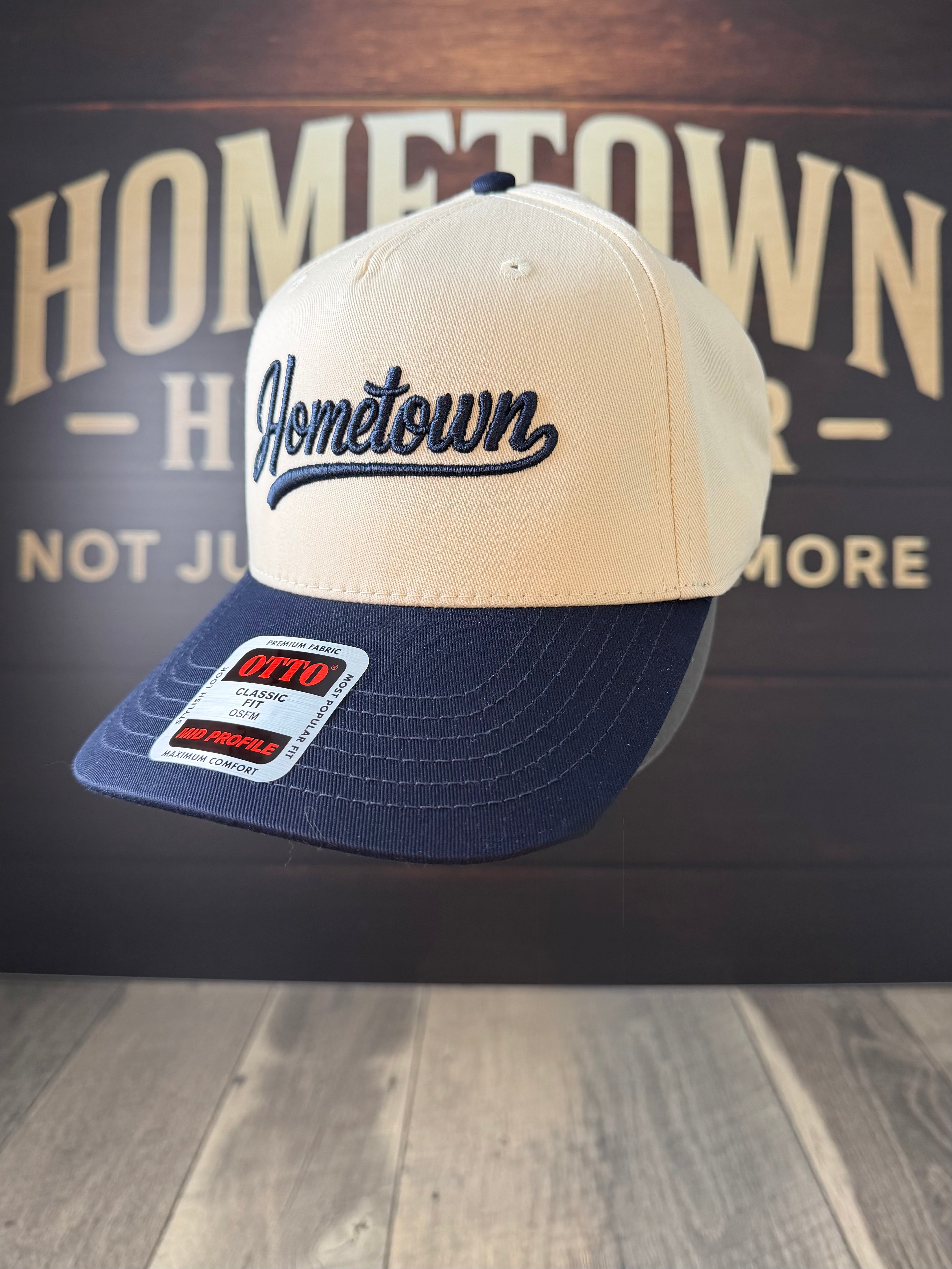 Beige and navy cap with 'Hometown' logo on a wooden surface and dark background.