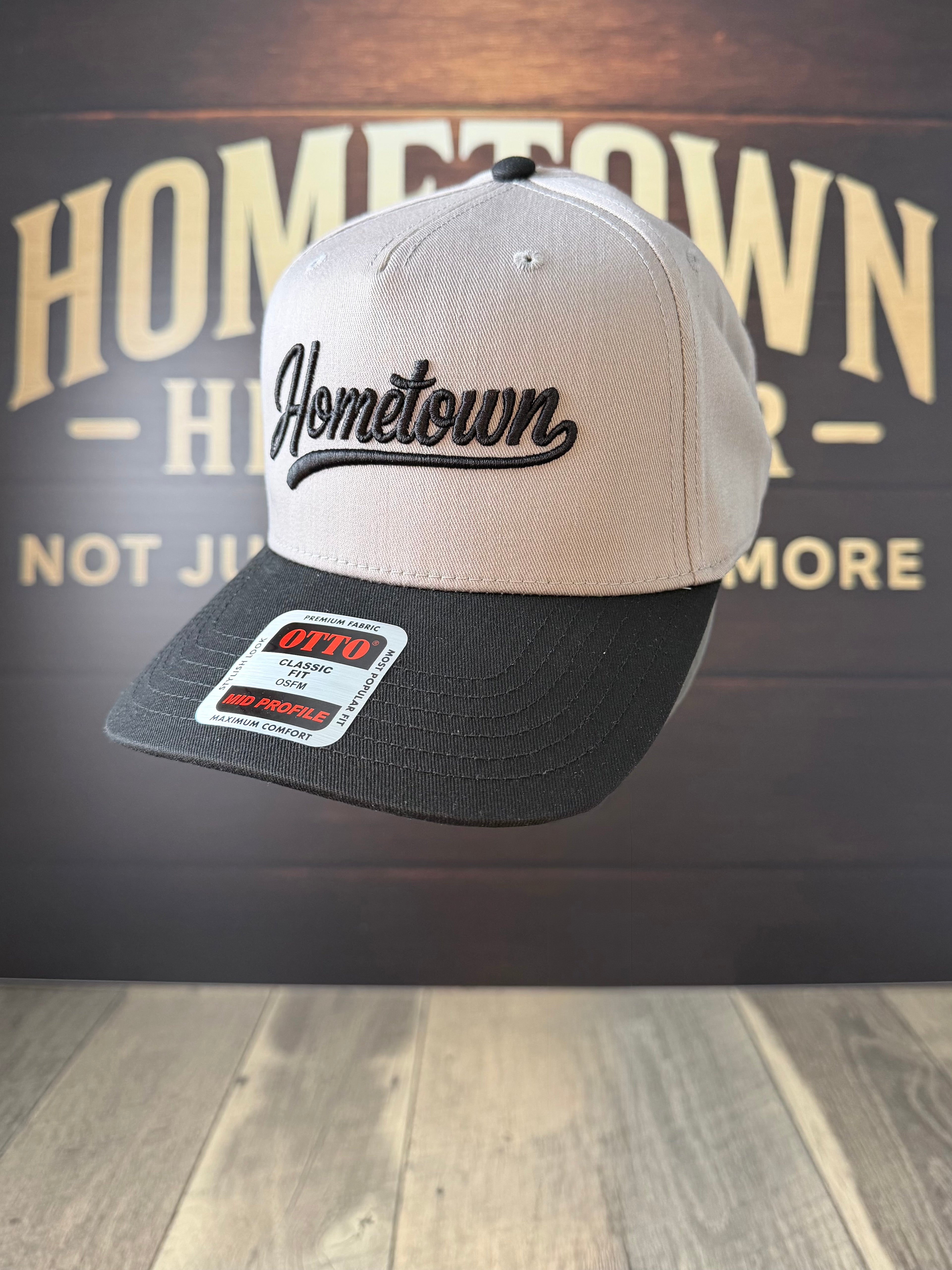 Two-tone cap with 'Hometown' logo on a wooden surface with 'Hometown' branding in the background.