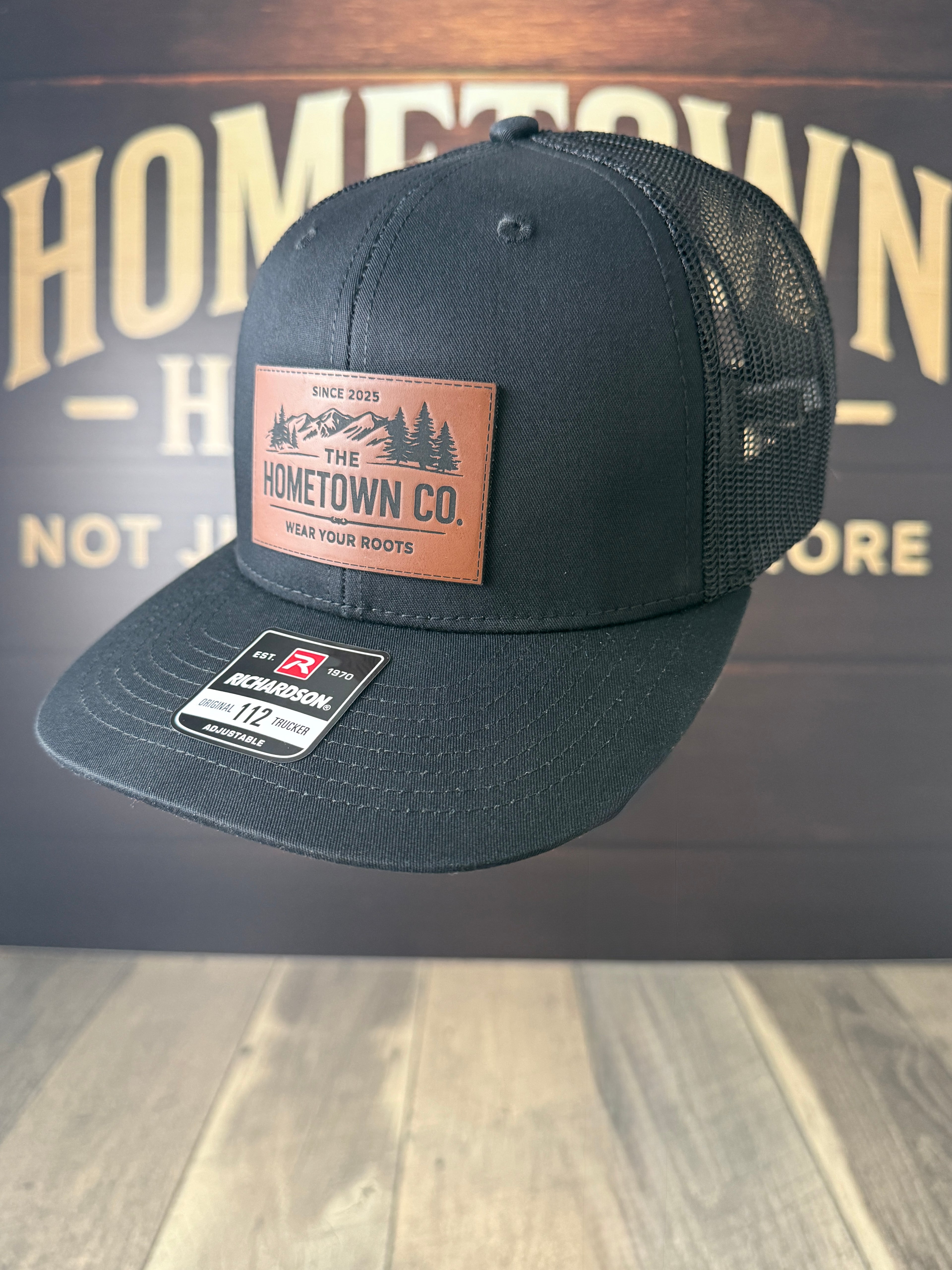 Black cap with a leather patch on a wooden surface with 'Hometown Co.' branding.