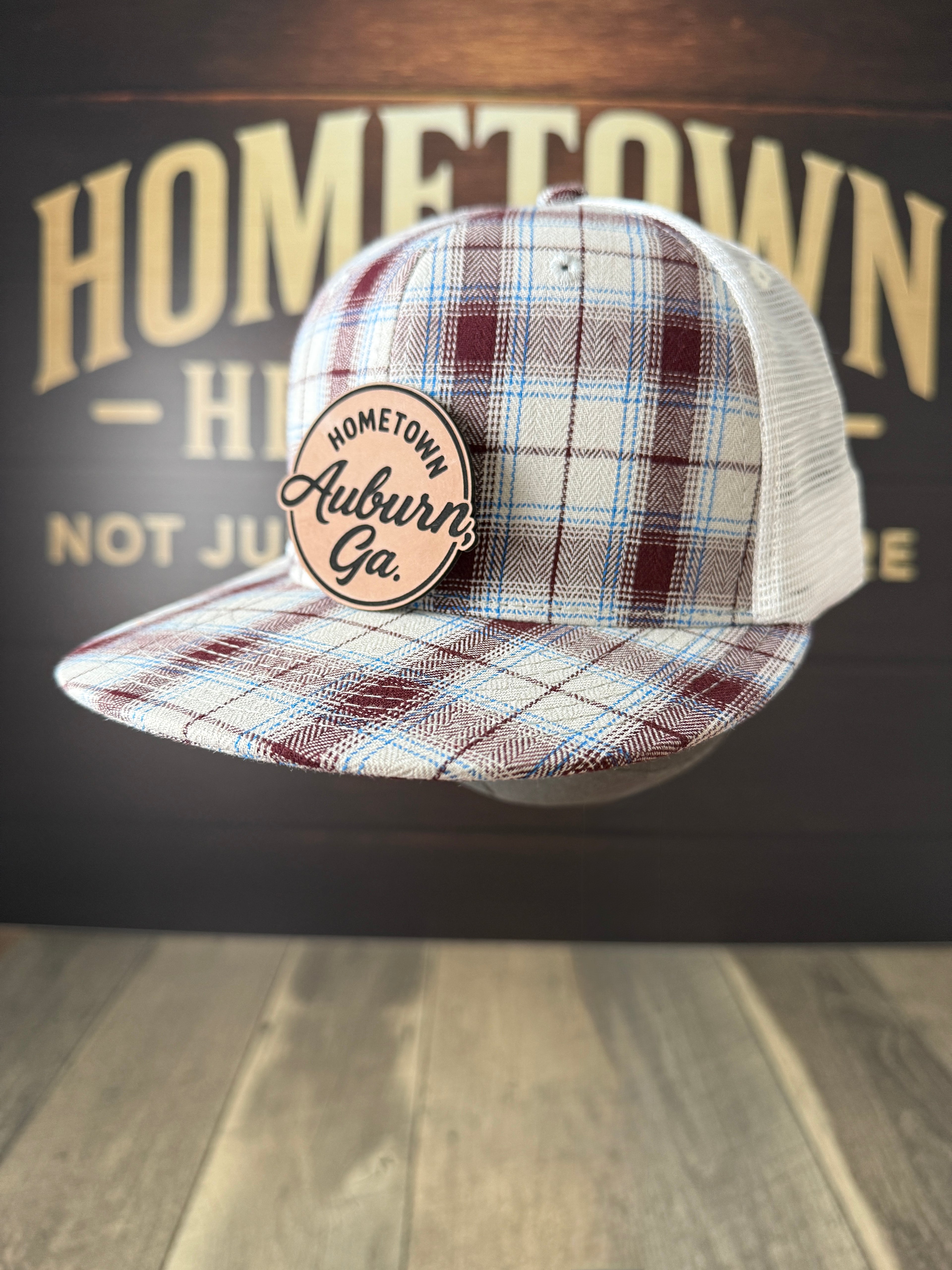 Plaid cap with 'Hometown Auburn, Ga.' badge on a wooden surface with 'Hometown' background.