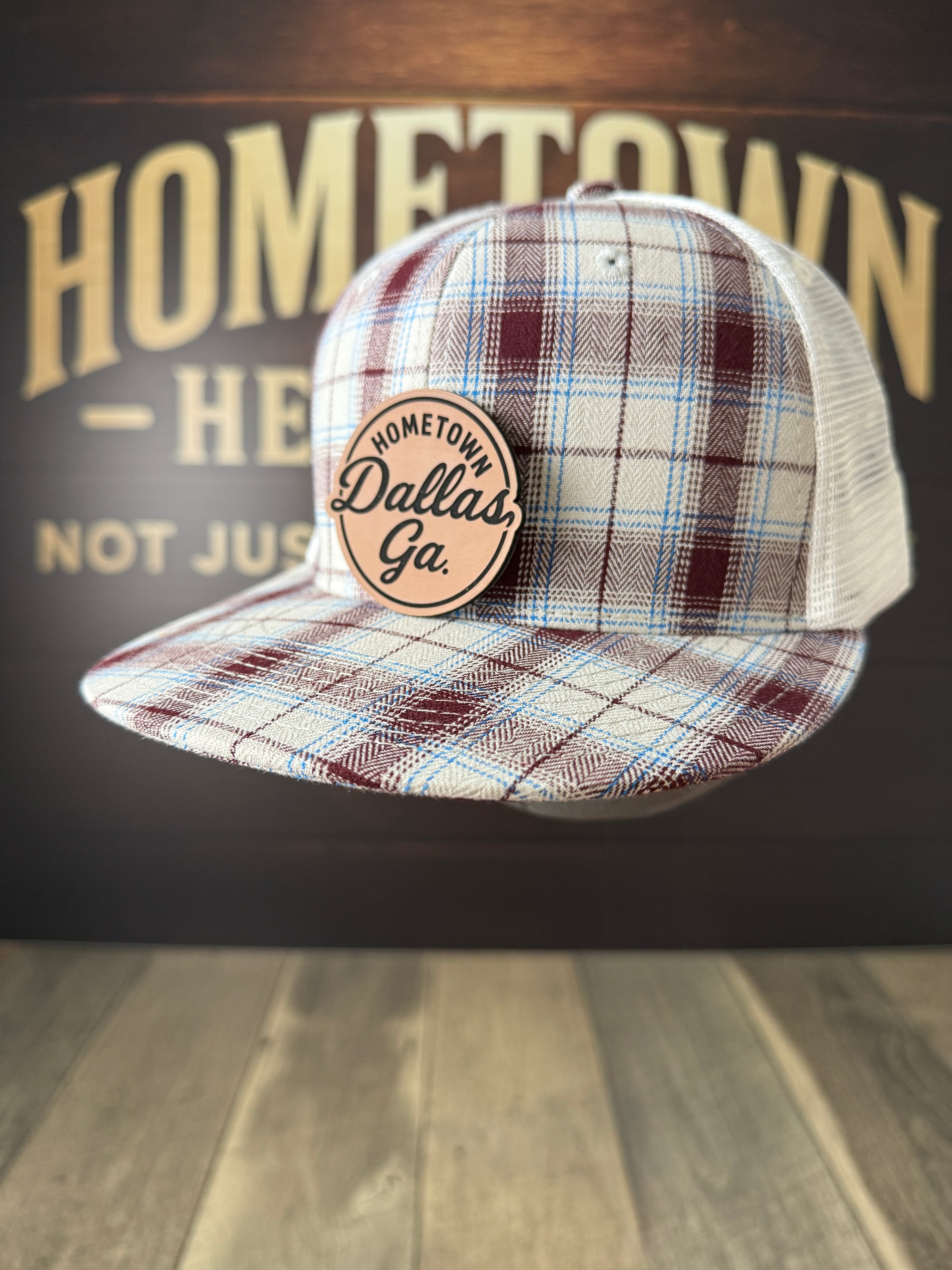Plaid cap with 'Hometown Dallas, Ga' patch against a wooden background