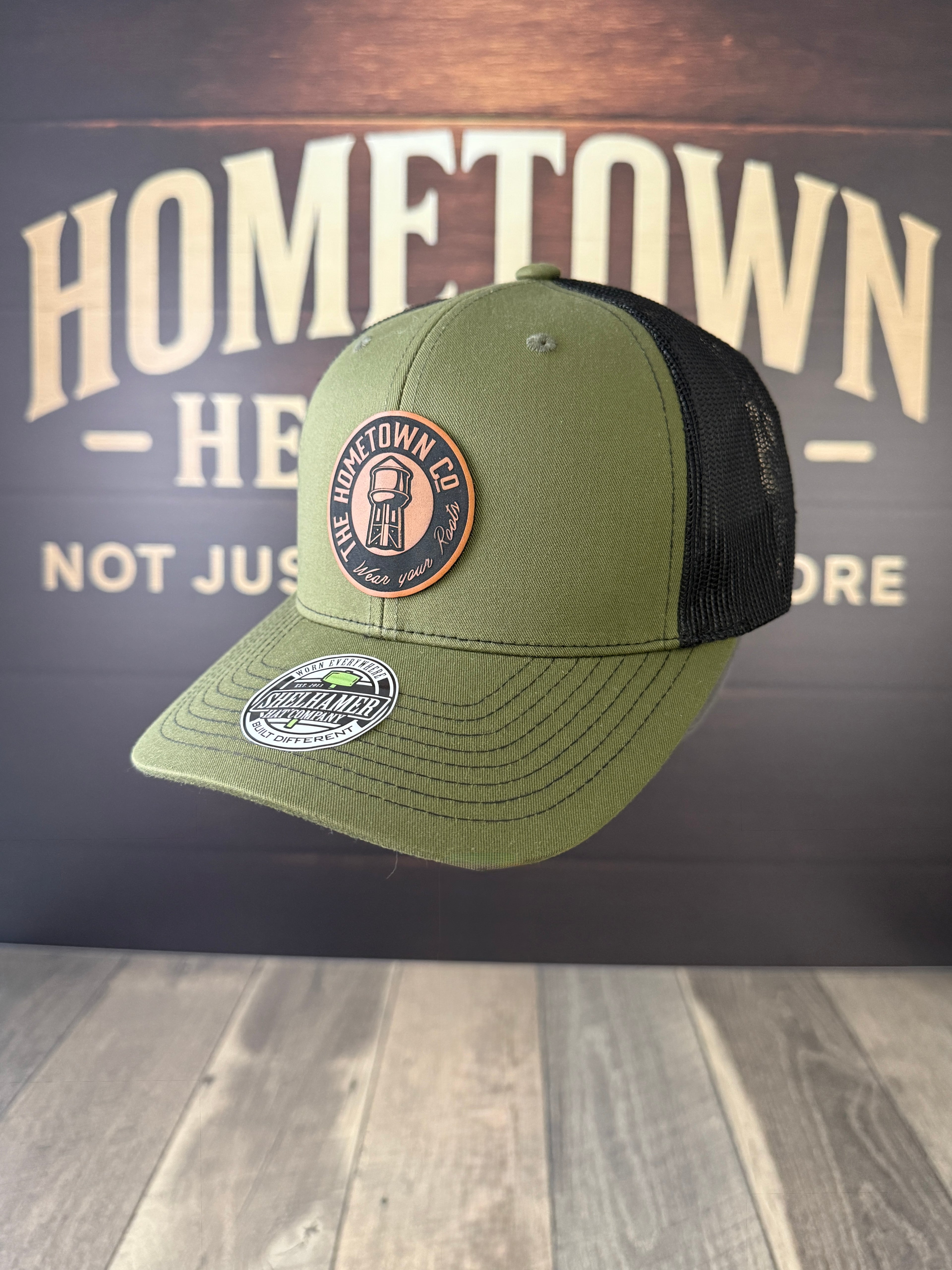 Green and black cap with patches on a wooden surface and dark background with 'Hometown' text.