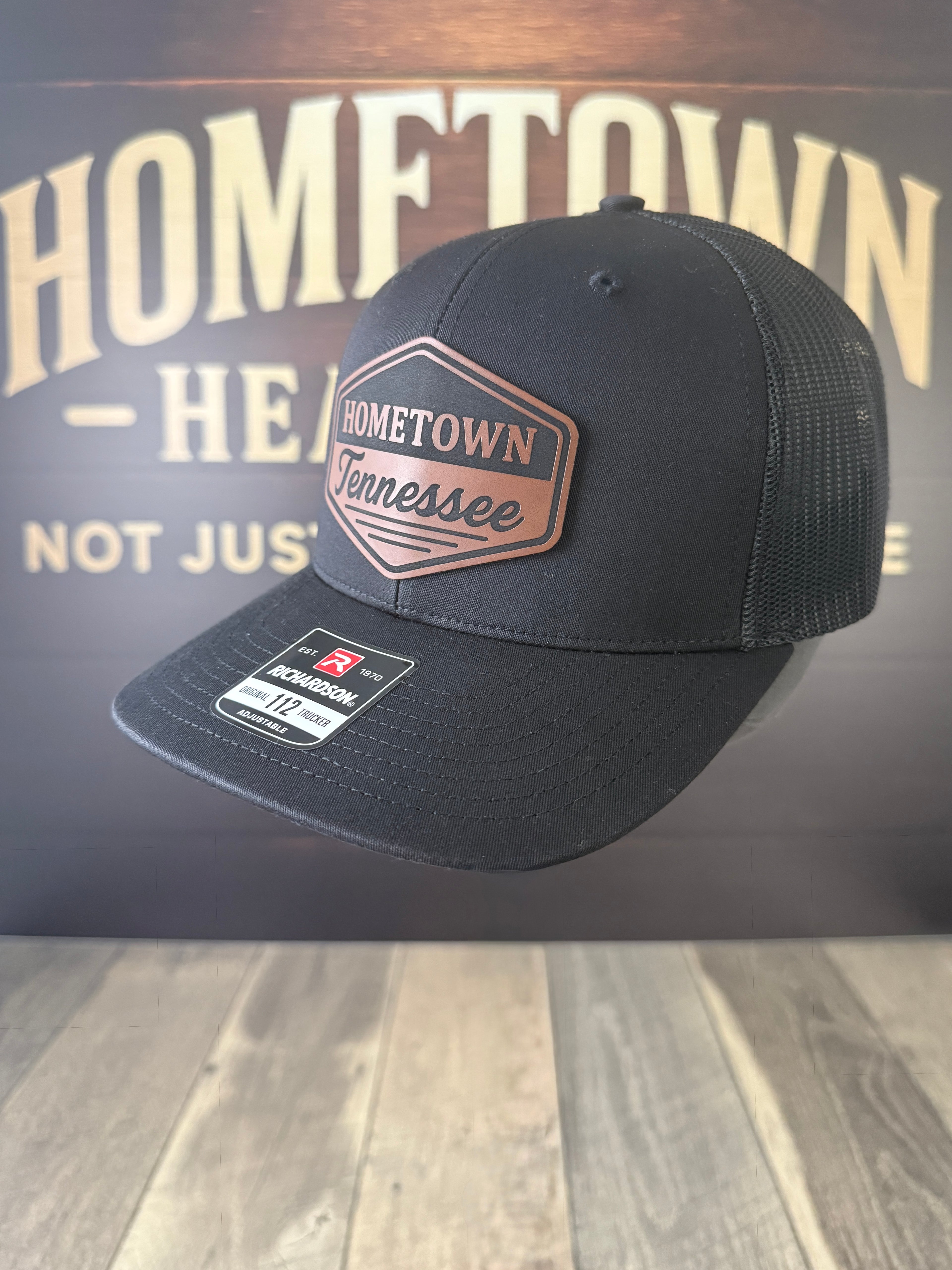 Black cap with 'Hometown Tennessee' logo on a wooden surface with 'Hometown' background