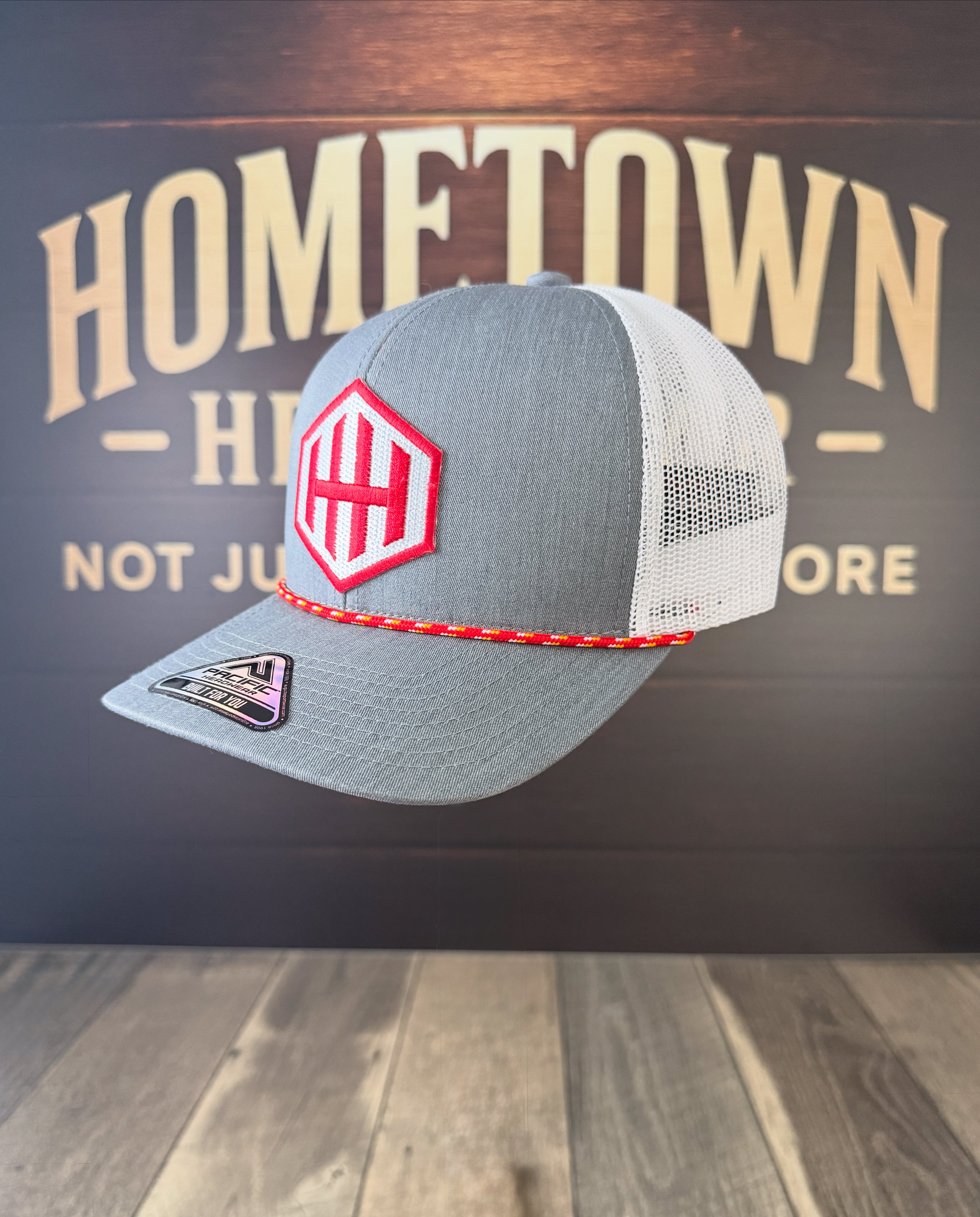 Gray and white cap with red logo on a wooden surface and dark background with 'Hometown' text.