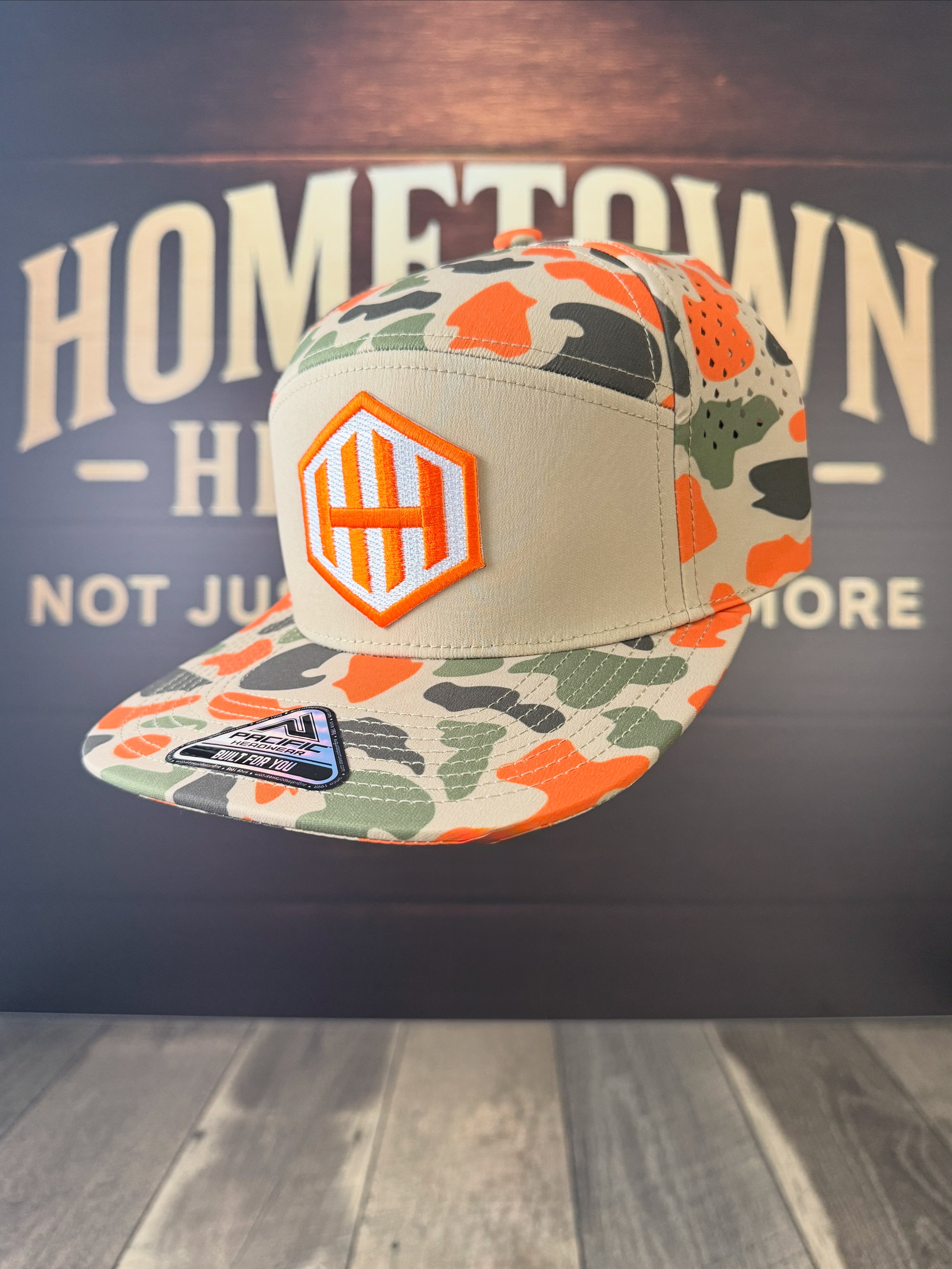 Camouflage cap with orange logo on a dark background with 'Hometown' text.