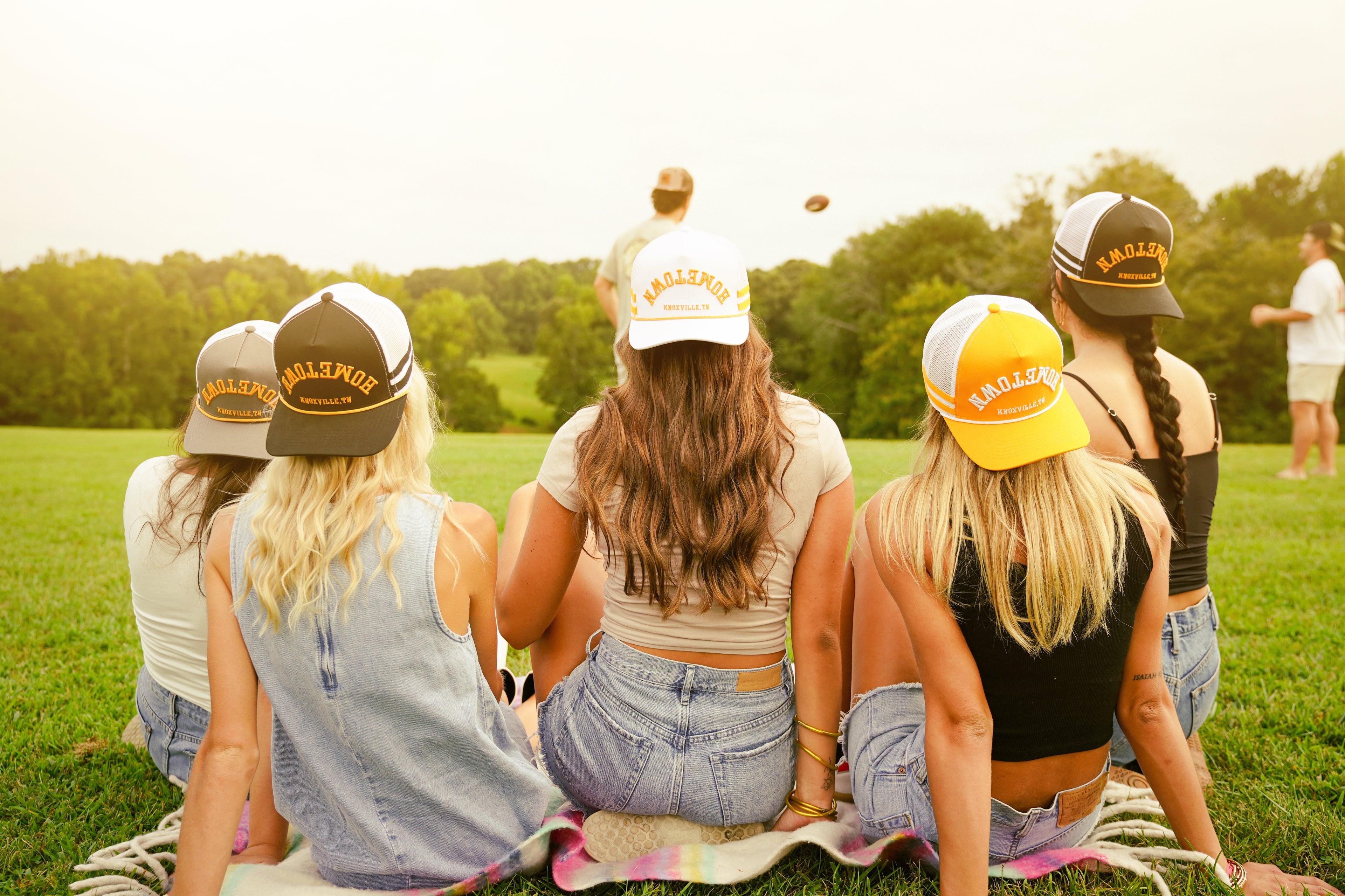 Group of women sitting on the grass wearing branded hats.